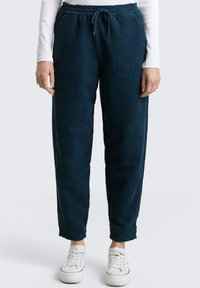 Donkerblauwe corduroy broek met een relaxte pasvorm, elastische tailleband, trekkoordsluiting en taps toelopende boorden, gecombineerd met witte sneakers.