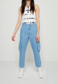 Jasnoniebieskie dżinsowe spodnie cargo z dwoma bocznymi kieszeniami, dopasowany krój, wysoki stan, w połączeniu z białym topem na ramiączkach z granatowymi paskami tie-dye.