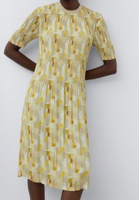 Šaty s krátkým rukávem vyrobené z lehkého, plisovaného materiálu s abstraktním vzorem v žluté, bílé a oranžové barvě a kulatým výstřihem.