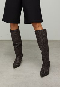 Bottes mi-mollet en matériau pailleté foncé avec bout pointu et talon fin ; design flexible avec une finition texturée.