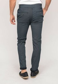 Pantalons à motifs bleus avec une coupe slim, dotés d'un ourlet roulé et de deux poches arrière avec des détails en bouton. Portés avec des chaussures sombres à enfiler.