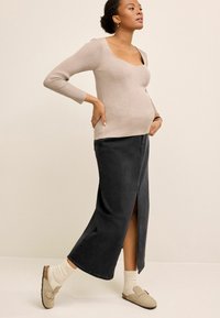 Beige bordás, hosszú ujjú pulóver négyzet alakú dekoltázzsal, sötét farmer maxi szoknyával párosítva, amely elülső hasítékkal rendelkezik. Földszínű slip-on cipők.