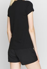 Camiseta de algodón negra con mangas cortas y escote redondo, combinada con pantalones cortos deportivos negros que tienen bolsillos laterales. Diseño simple y limpio.