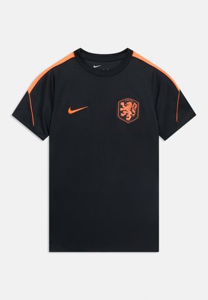 Maglietta sportiva nera a maniche corte con strisce arancioni sulle spalle, logo Nike e uno stemma con un emblema di leone sul petto sinistro.