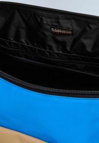 Intérieur d'un sac en tissu bleu et beige avec un revêtement noir, doté d'une fermeture éclair et d'une petite étiquette noire portant la marque "Napapijri".