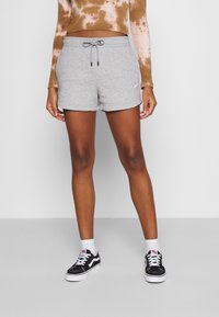 Grå träningsshorts i mjukt material med dragsko i midjan och sidofickor, med en liten lila Nike-logotyp på vänster sida.