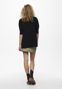 Svart långärmad topp med texturerad tyg, tillsammans med en beige kjol och svarta ankelstövlar med kraftiga sulor.