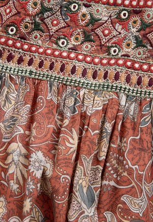 Red and beige patterned fabric with floral motifs, detailed with multi-colored embroidery along the hem and decorative stitching elements.