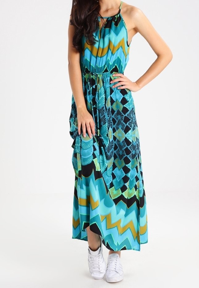 Robe longue en tissu bleu-vert avec motifs géométriques, col halter, taille cintrée et jupe à volants, associée à des baskets blanches.