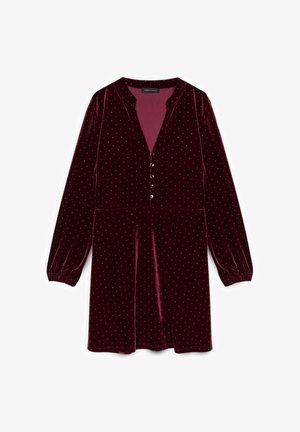 Burgunderrød fløjlskjole med lange ærmer, knaplukning foran og sølvpunkter. Har en v-udskæring og samlede ærmeafslutninger.