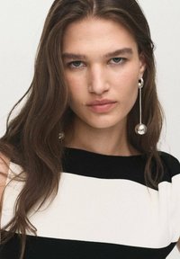Black and white striped top with a high neckline. Long silver earrings featuring round, reflective balls. Smooth hair texture around the face.