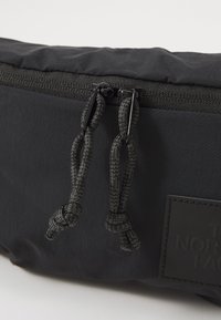 Black fabric bag with zip closure, featuring braided pull cords and a textured rectangular label embossed with "The North Face."