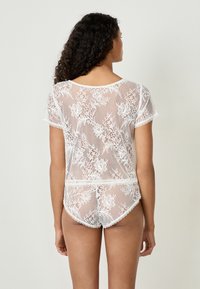 Wit kanten lingeriesetje met bloemenpatronen, korte mouwen en scalloped randen, dat een semi-doorzichtige textuur en een getailleerd ontwerp laat zien.