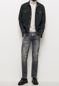 Camisa de mezclilla oscura con dos bolsillos en el pecho, combinada con jeans grises y zapatos negros con cordones, sobre un fondo neutral.