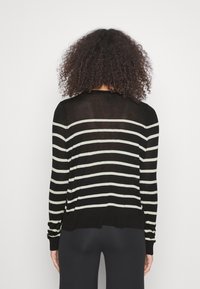 Pull à rayures noires à manches longues, avec des rayures horizontales couleur crème, un col rond et une coupe décontractée. Tissu tricoté texturé.