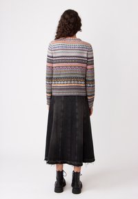 Maglione lavorato a maglia multicolore con motivi vari, abbinato a una lunga gonna di jeans nera con orlo sfrangiato e cuciture verticali.