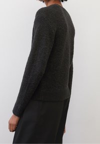 Pull gris foncé en tricot avec une surface texturée, col rond, ourlet et poignets côtelés. Présenté de profil, rentré dans un pantalon noir.