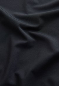 Tissu noir lisse avec une texture côtelée diagonale subtile et des plis doux créant des ombres et des reflets délicats.
