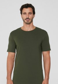 Oliwkowy t-shirt z krótkim rękawem, wykonany z miękkiego, lekkiego materiału. Posiada okrągły dekolt oraz luźny krój z minimalnymi detalami ściegów.