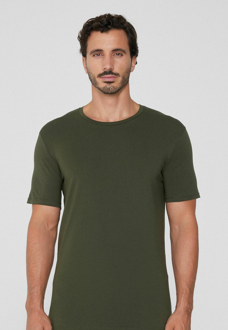 Oliwkowy t-shirt z krótkim rękawem, wykonany z miękkiego, lekkiego materiału. Posiada okrągły dekolt oraz luźny krój z minimalnymi detalami ściegów.