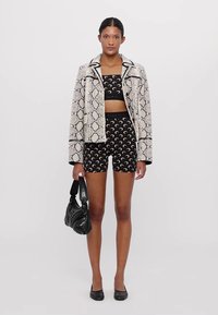 Slangebilde mønsteret cropped blazer, svart crop topp og shorts med halvmåne mønster, svart håndveske og lave hæler.