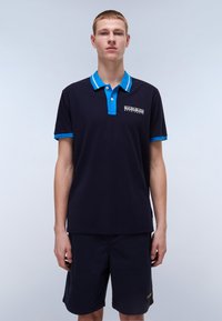Marine blå poloskjorte med blå krage og mansjetter, med et logo på venstre bryst. Bæres med mørke shorts, glatte teksturer, uformell design.
