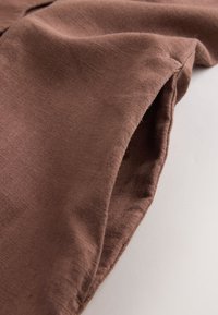 Lähikuva ruskeasta kangashihasta, jossa näkyy ompeleiden sauma vaalealla taustalla.