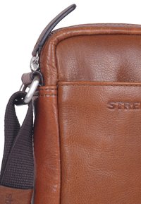 Borsa a spalla in pelle marrone con una consistenza morbida, dotata di una zip argento e di una tracolla in tessuto scuro, con dettagli del marchio impressi sul lato.