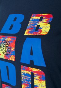 Laivansinis t-paita, jossa on suuria, rohkeita sinisiä, punaisia ja keltaisia kirjaimia, joissa on tekstuurinen muotoilu ja pyöreä leijonasarvi.