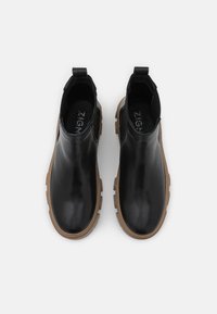 Botas de cuero negro hasta el tobillo con un acabado suave, paneles laterales elásticos y suelas de goma beige con textura que ofrecen agarre.
