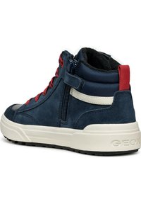 Sneaker alta con una finitura in suede blu navy, lacci rossi e accenti bianchi. Presenta una chiusura con zip e una suola testurizzata per una presa migliorata.