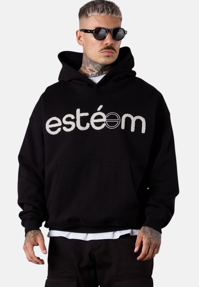 Un hoodie noir avec une poche avant présentant le texte brodé en blanc "estéem." Le tissu semble doux, avec une coupe décontractée et une capuche ajustable.