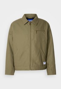 Veste verte olive avec fermeture éclair, col pointu, poche poitrine simple, poches latérales et étiquette de la marque bleue sur l'ourlet.