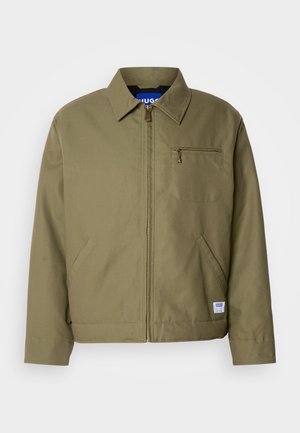Giacca verde oliva con chiusura a zip, colletto a punta, taschino sul petto, tasche laterali e etichetta blu del marchio sull'orlo.