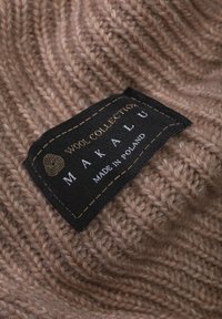 Kolorowa, dziana wełniana tkanina w jasnobrązowym kolorze z teksturowanym, prążkowanym wzorem. Zawiera czarną metkę z napisem "Makala" i "Wyprodukowano w Polsce".