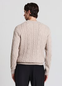 Hellbeiger Strickpullover mit Zopfmuster, gerippten Bündchen und Saum, mit texturierter Struktur. Dazu schwarze Hose mit figurbetontem Schnitt.