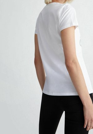 Bílé bavlněné tričko s krátkým rukávem, kulatým výstřihem a přiléhavým střihem. Hladká textura a žádné viditelné vzory nebo ozdoby.