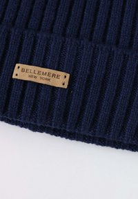 Navy ribbed knit hat featuring a beige leather label with embossed text "BELLEMEIRE NEW YORK" and decorative stitching details.