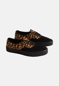 Par de zapatillas Vans negras y con estampado de leopardo, con suelas de goma negras y cordones, colocadas una al lado de la otra sobre un fondo blanco.