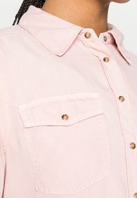 Lichtroze overhemd met knopen, voorzien van een kraag, metalen drukknoopsluitingen en een borstzak met een afgeronde klep. Soepele stoftextuur.