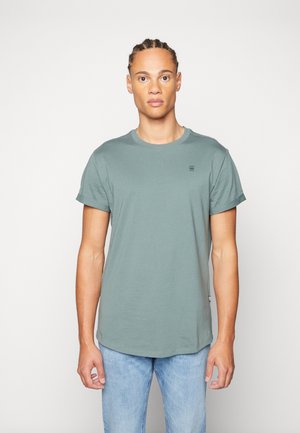 Green short-sleeved t-shirt made of cotton, featuring a crew neck and a small logo on the chest; paired with light blue denim jeans.