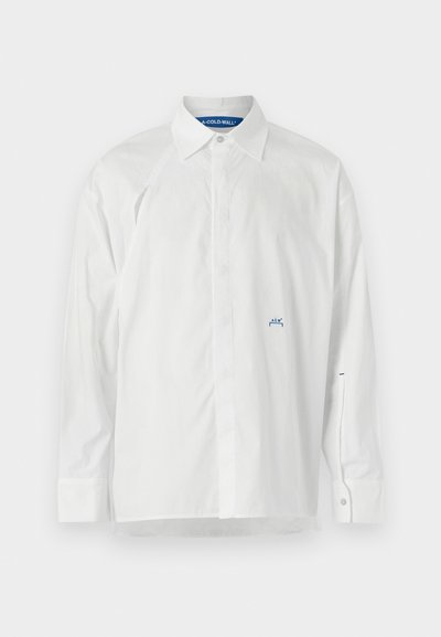 Chemise blanche à manches longues en coton. Elle présente un col pointu, une fermeture à boutons et un logo bleu sur la poitrine et la manche. Texture douce.