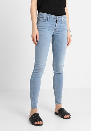 Jeans ajustados de color azul claro, fabricados en denim, con cintura de altura media, diseño de cinco bolsillos y un ajuste ceñido en las piernas.