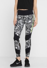 Leggings con motivo in bianco e nero presentano una combinazione di disegni floreali e pannelli neri solidi. Un accento verde neon corre lungo il lato.