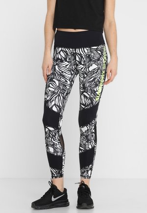 Zwart-wit gestreepte leggings hebben een mix van bloemmotieven en stevige zwarte panelen. Een neon groene accent loopt langs de zijkant.