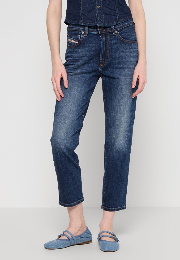 Donna che indossa jeans in denim blu scuro e un top senza maniche in denim coordinato, abbinati a scarpe Mary Jane blu chiaro.