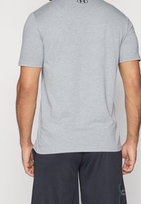 Grå kortærmet T-shirt med en glat tekstur, der har et logo på nakken og en klassisk pasform, parret med sorte shorts.
