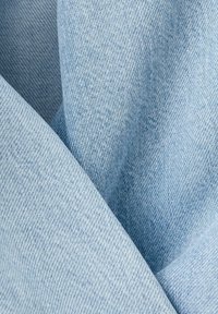 Gros plan sur un tissu en denim bleu clair montrant un tissage serré et des plis subtils, mettant en valeur la texture et la qualité du matériau.