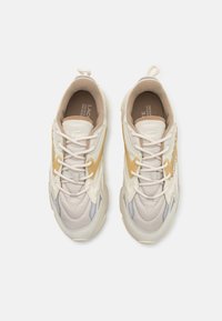 Beige and cream sneakers with a textured upper, featuring a yellow accent and gray detailing, laced with flat white shoelaces.