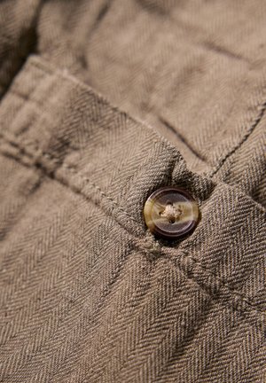 Brown herringbone fabric close-up with a round, dark button and visible stitching details. The texture appears soft and woven.